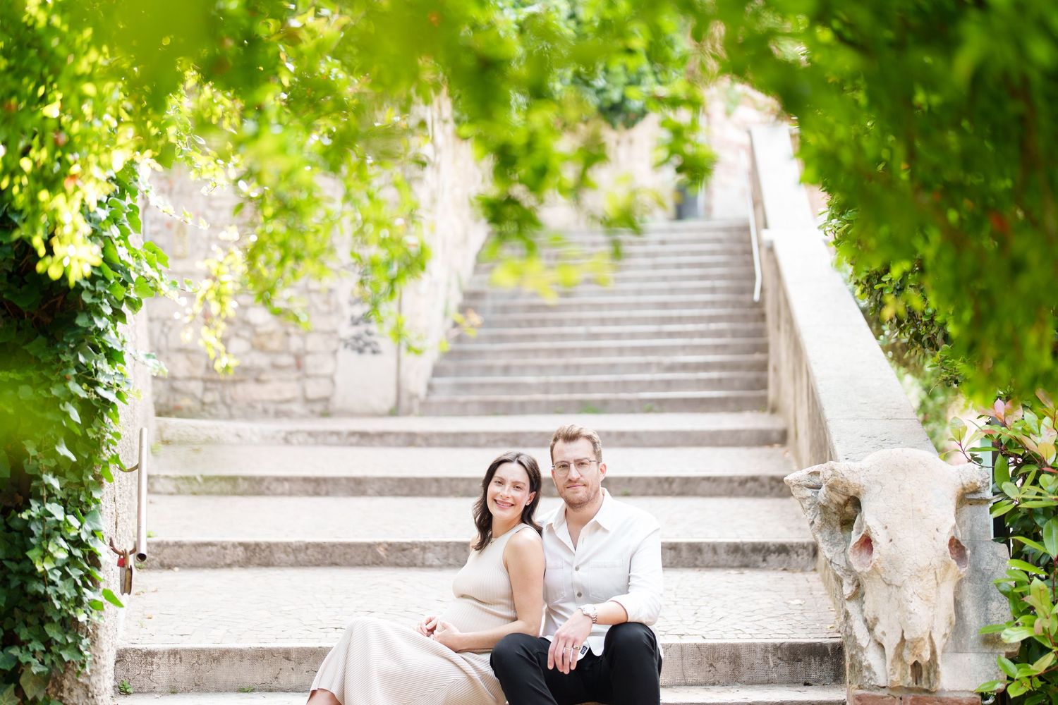 Couple sharing a romantic moment on stone steps surrounded by green foliage in a garden setting.