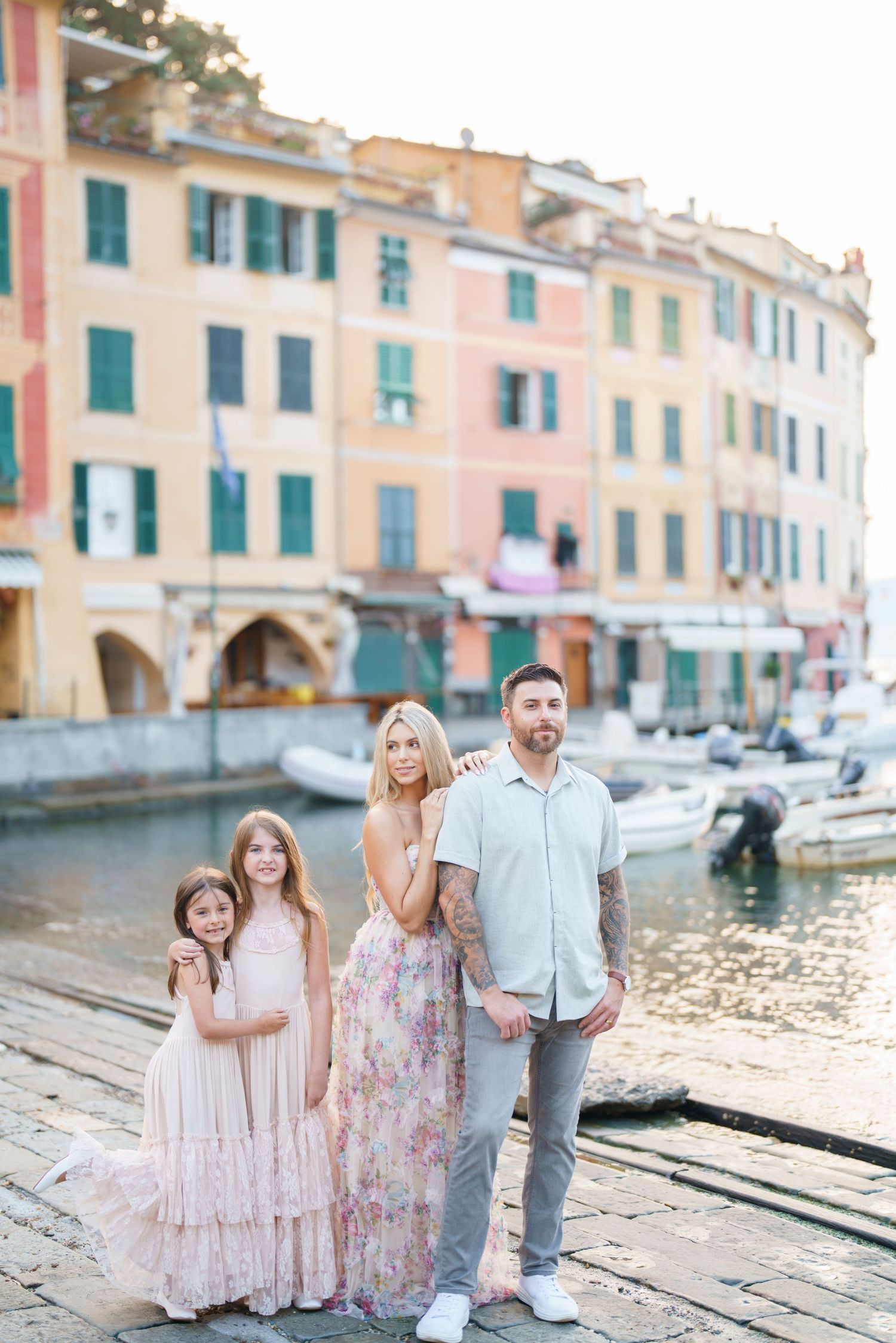 Family standing together by boats in Portofino harbor with colorful Italian buildings in background at sunset.