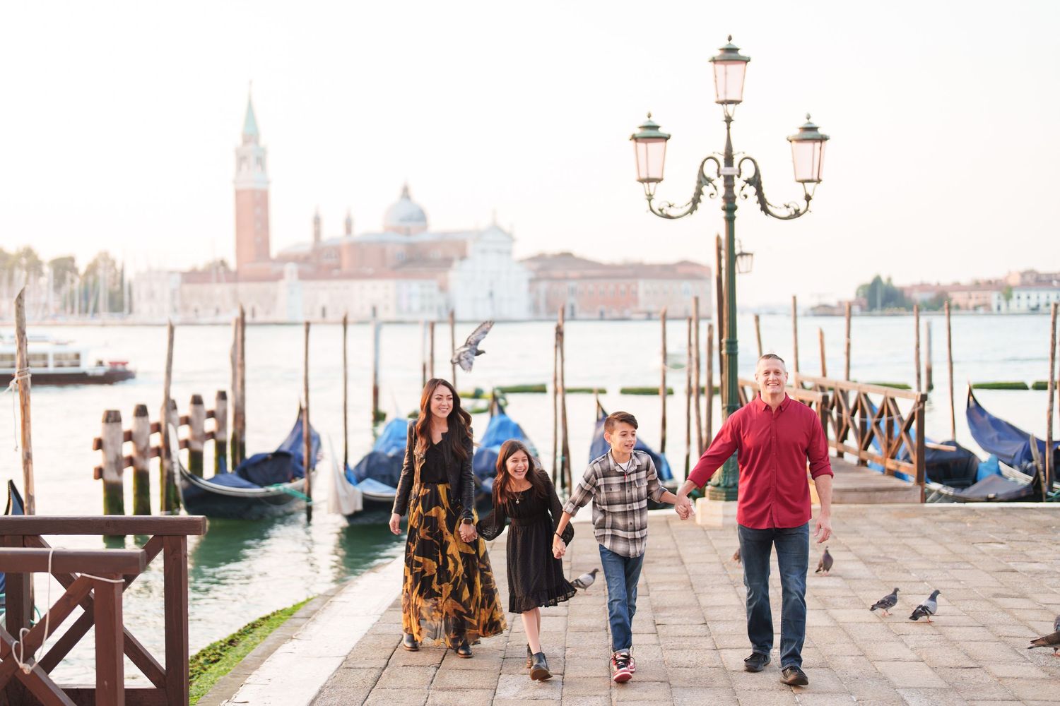Family walking along Venice waterfront promenade with gondolas and San Giorgio Maggiore church in background.