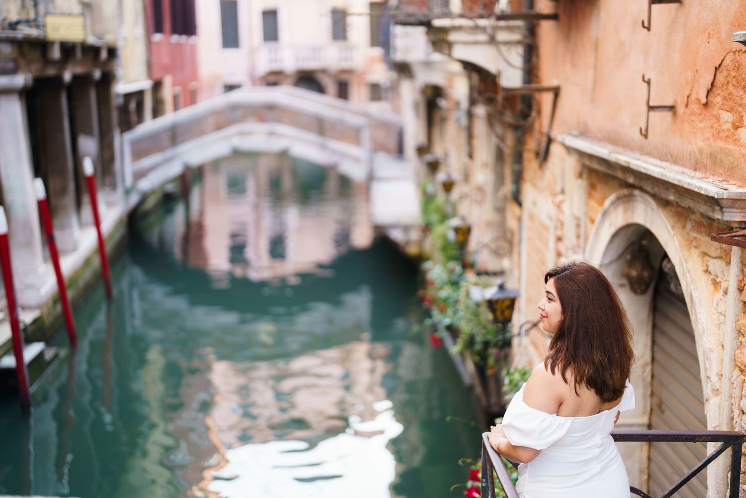 Person in white dress admiring scenic Venice canal view with bridge and historic buildings in background.