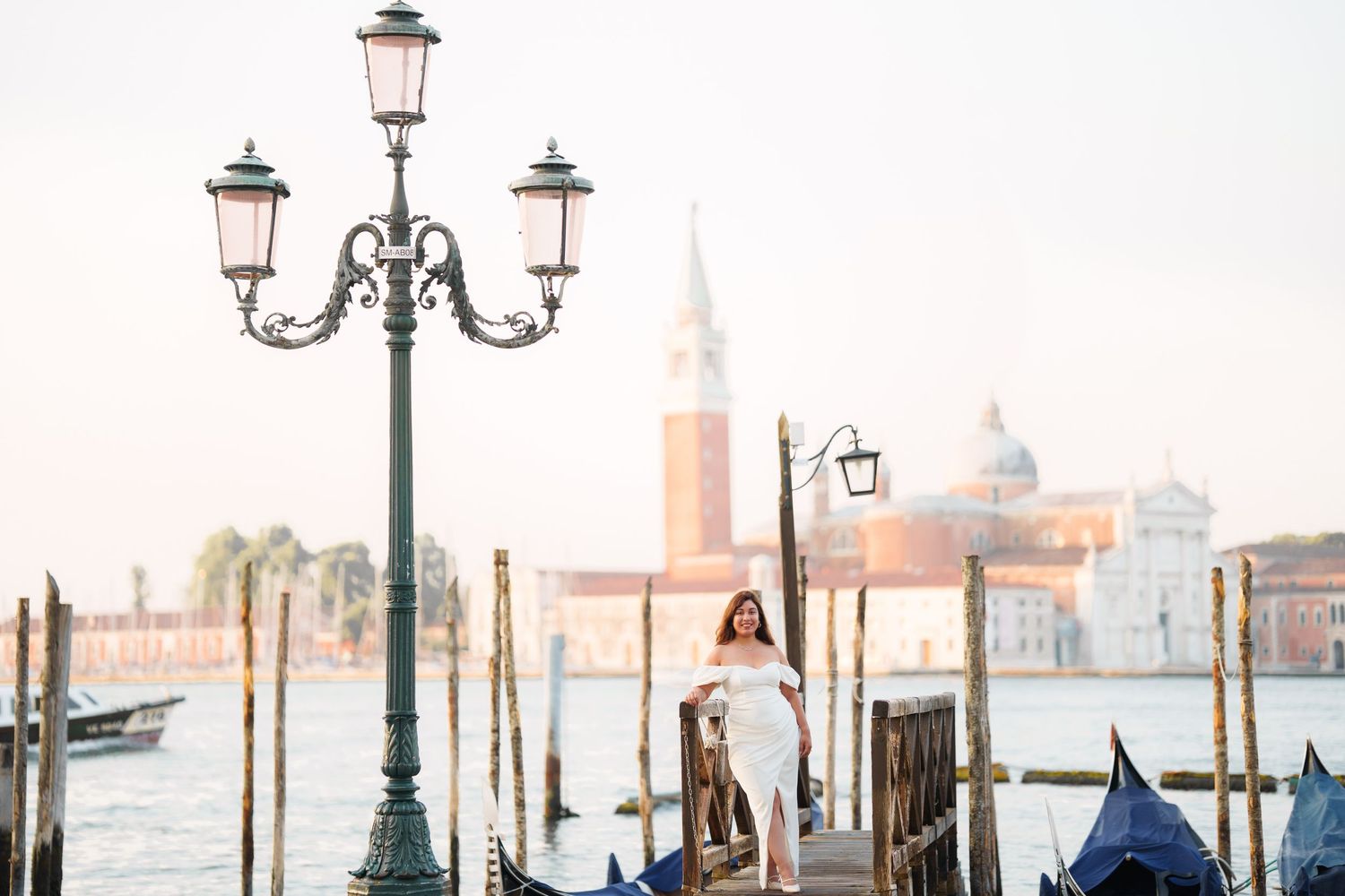 photographer venicePerson stands by ornate lamppost near gondolas in Venice with San Giorgio Maggiore church in background.