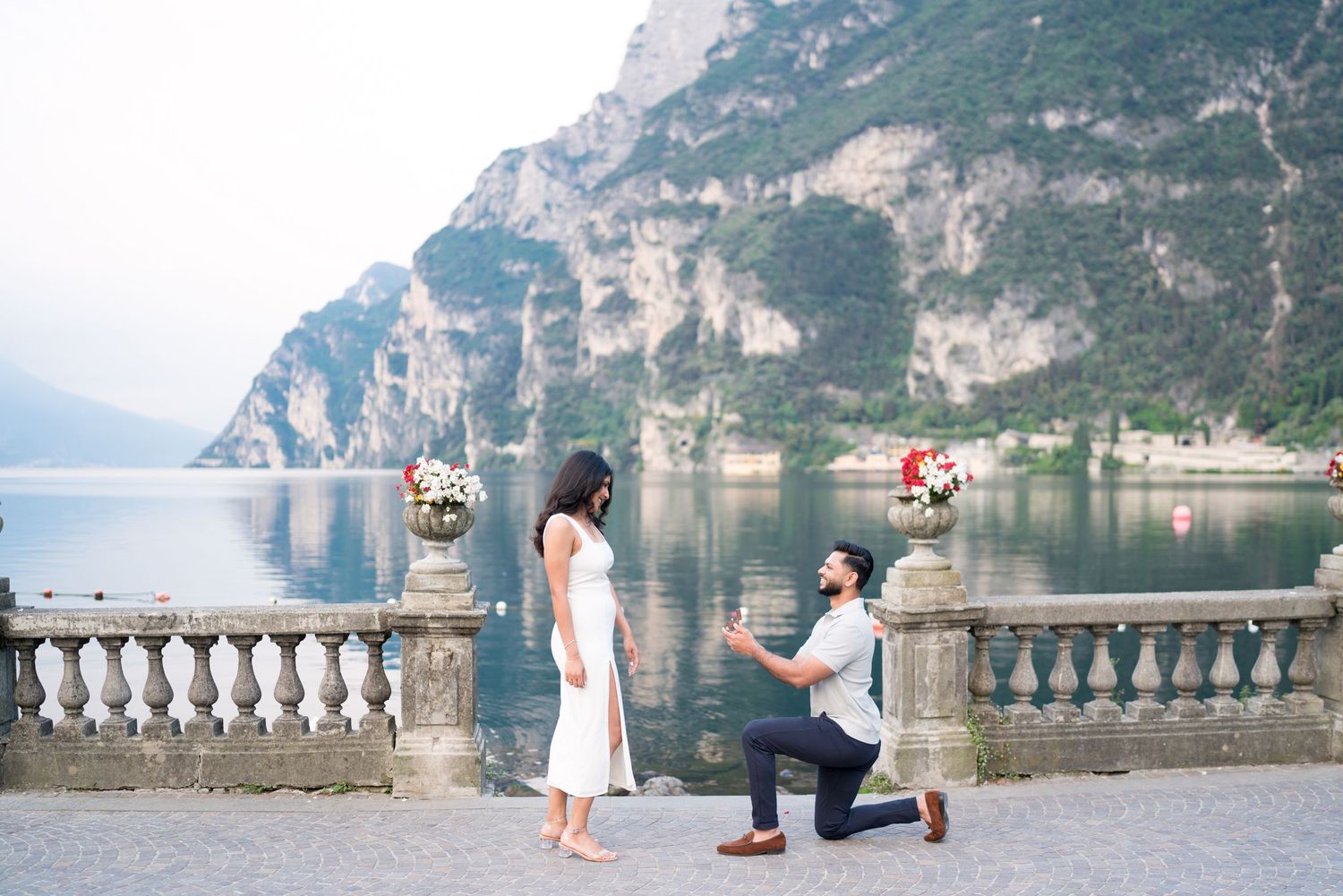 A romantic proposal moment on a scenic balcony overlooking Lake Garda in Italy with mountains in the background.