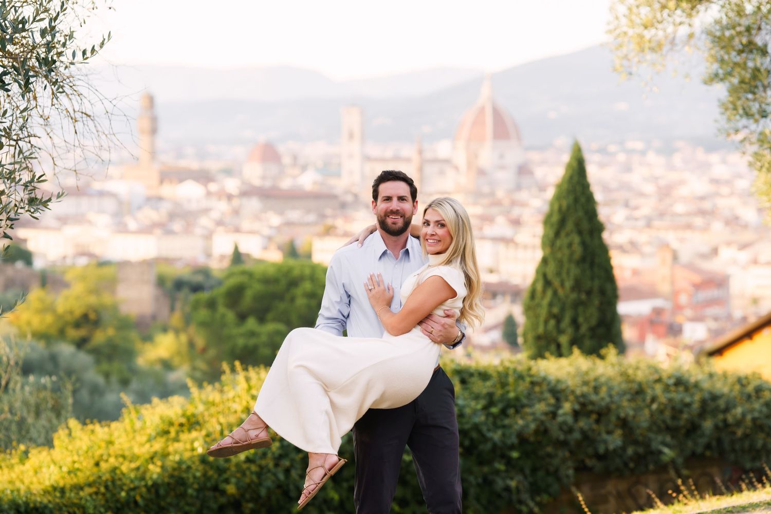 A romantic couple embraces during a sunset photoshoot overlooking Florence, Italy with the Duomo cathedral visible in background.