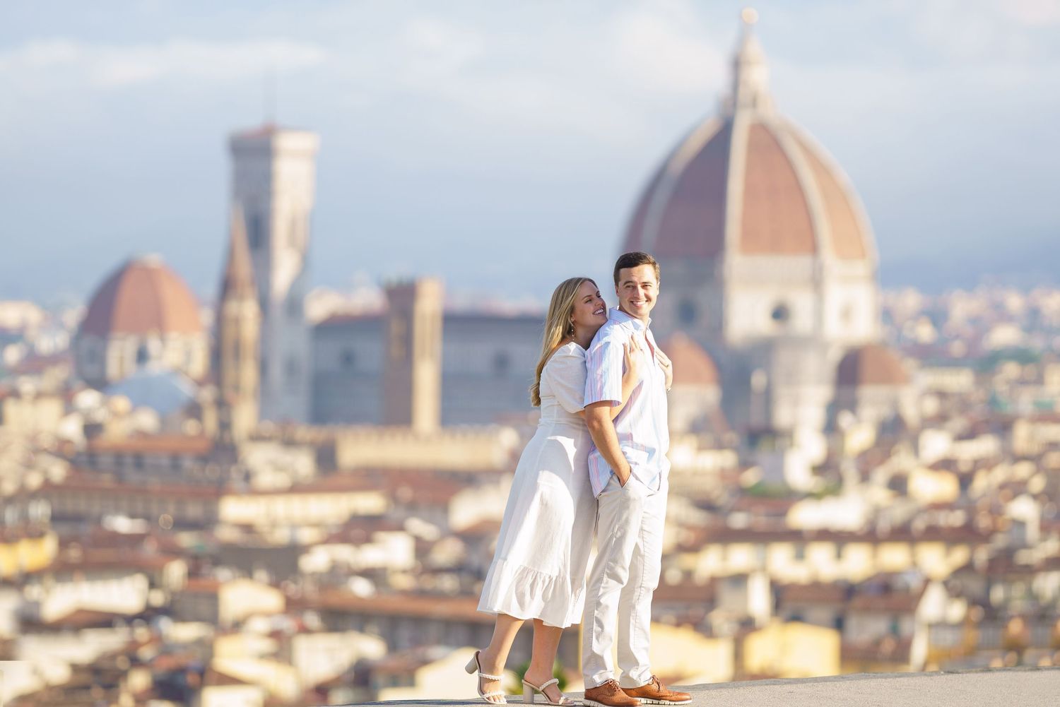 Two people in white outfits stand on a viewpoint overlooking Florence with the iconic Duomo cathedral in the background.
