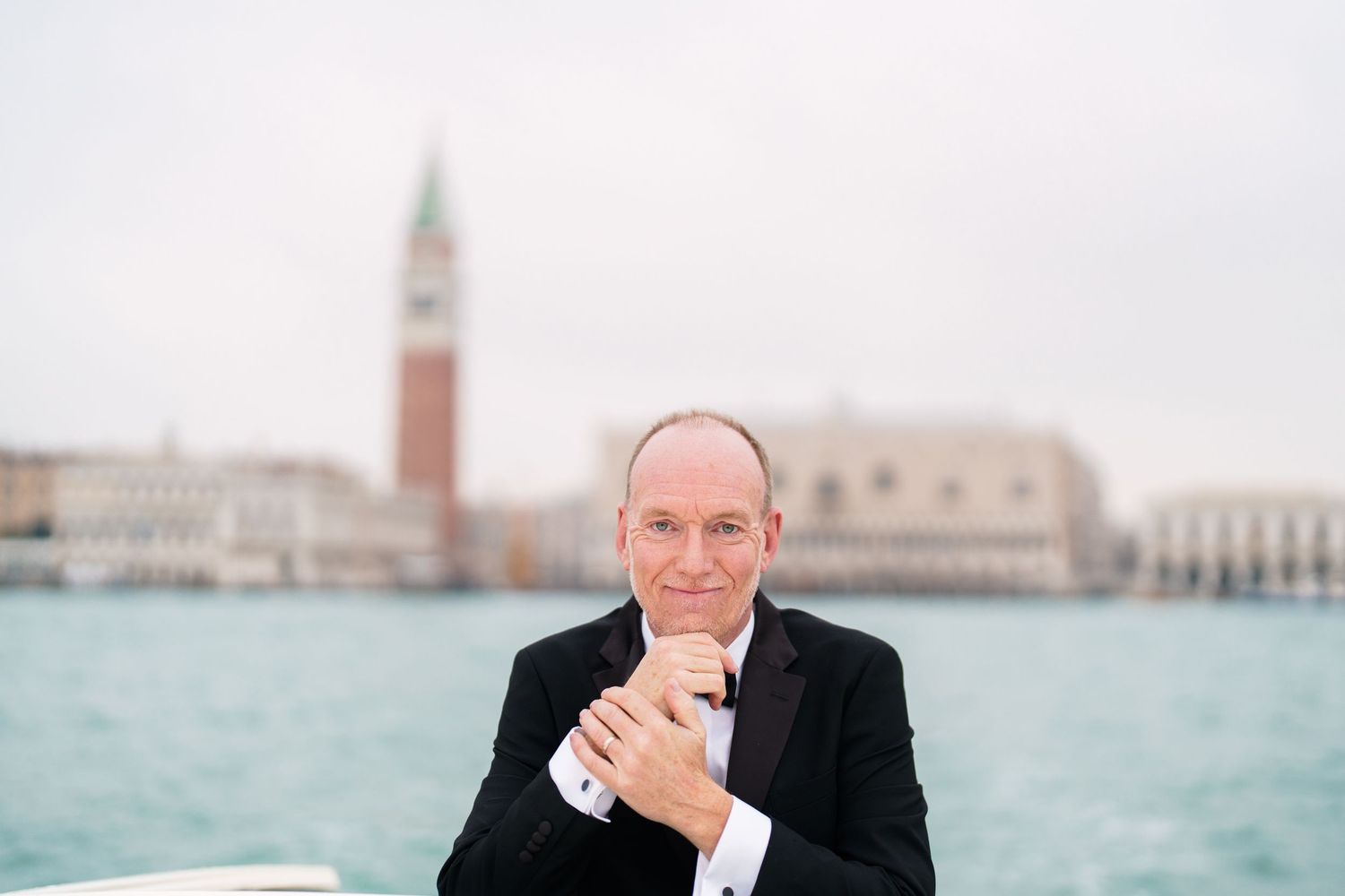 Person in formal attire poses for photos with Venice's iconic Saint Mark's Square and lagoon in the background.
