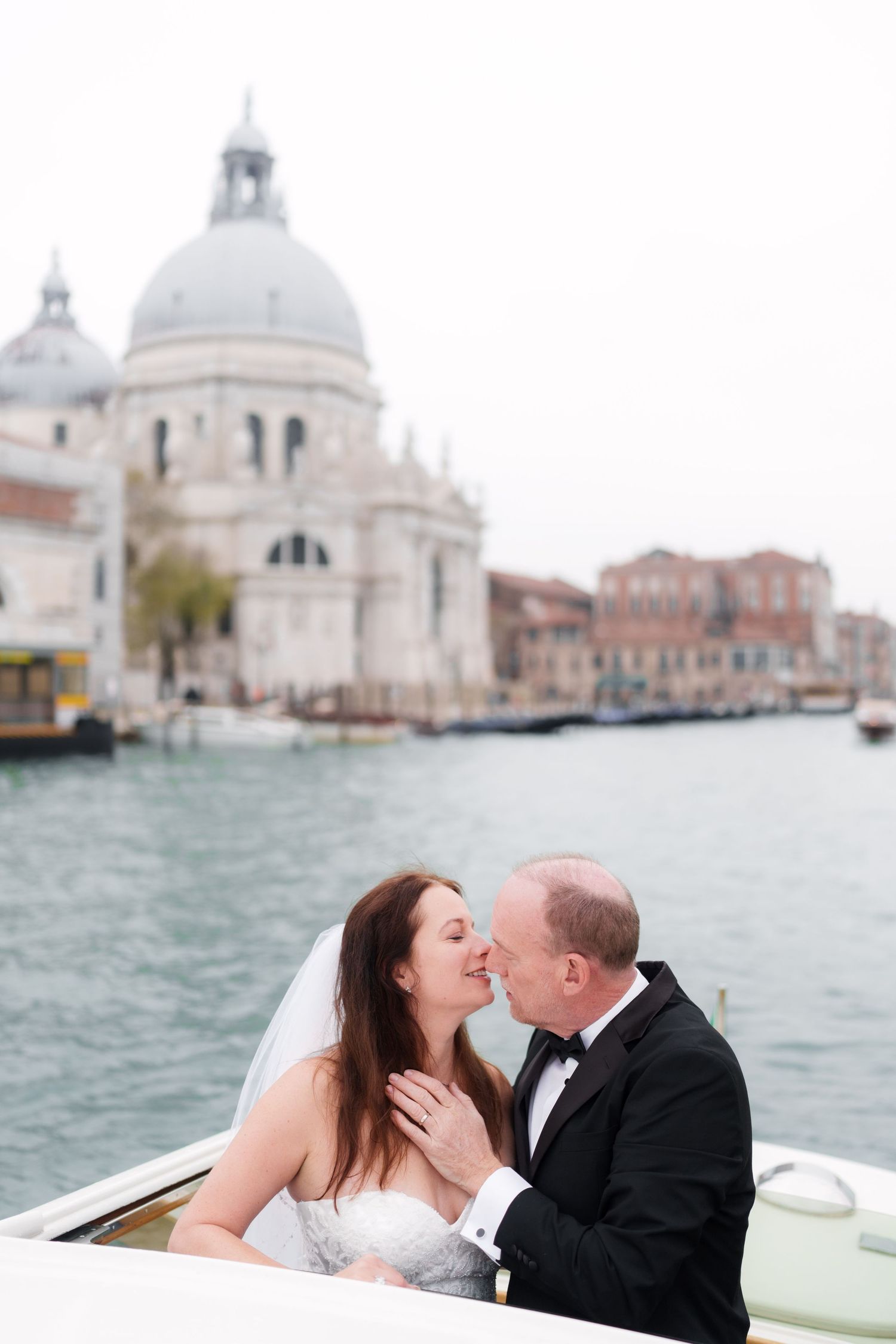 Romantic couple sharing intimate moments in a boat on Venice's Grand Canal with the Santa Maria della Salute dome in background.