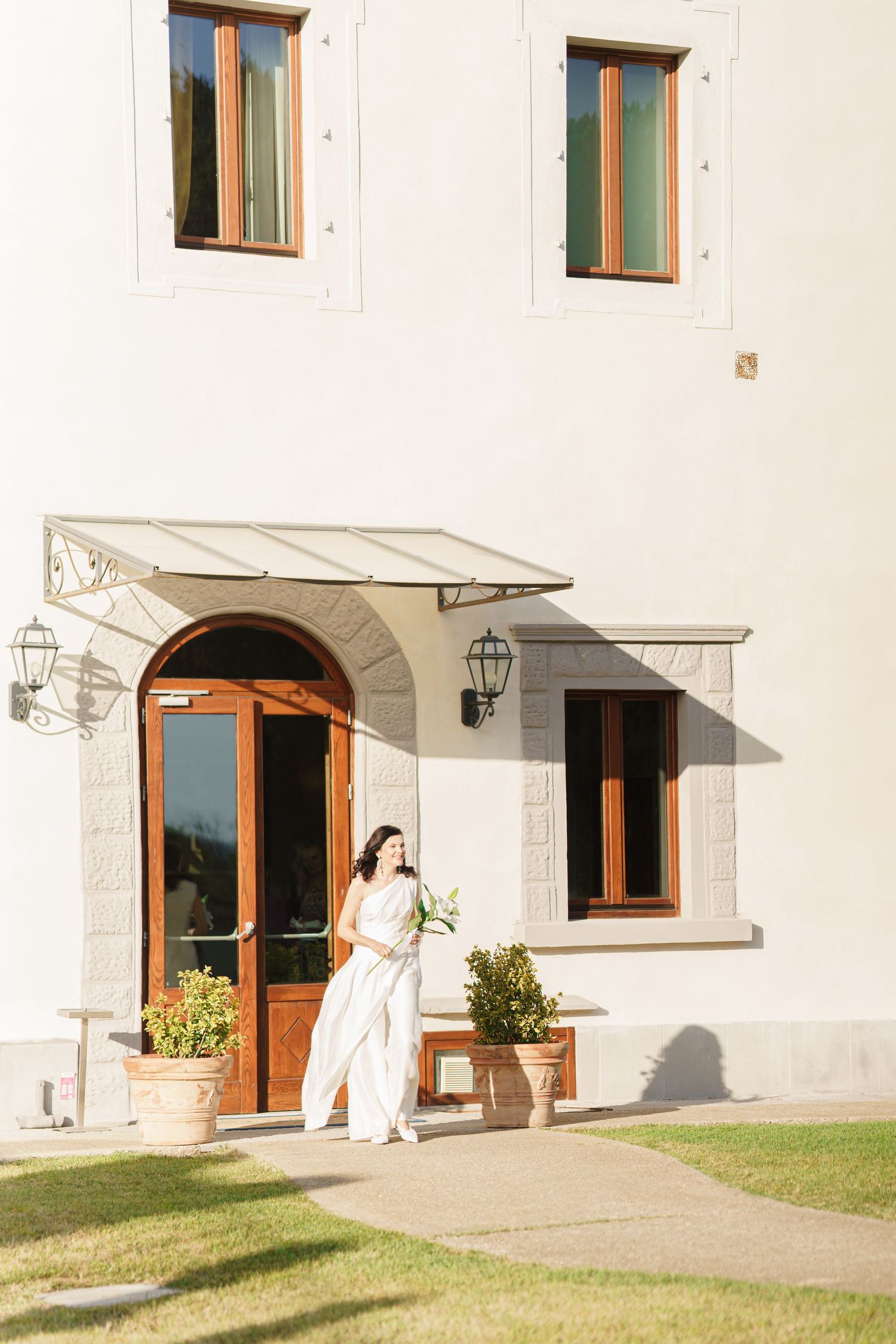 White building exterior with wooden windows and arched doorways in sunlight.