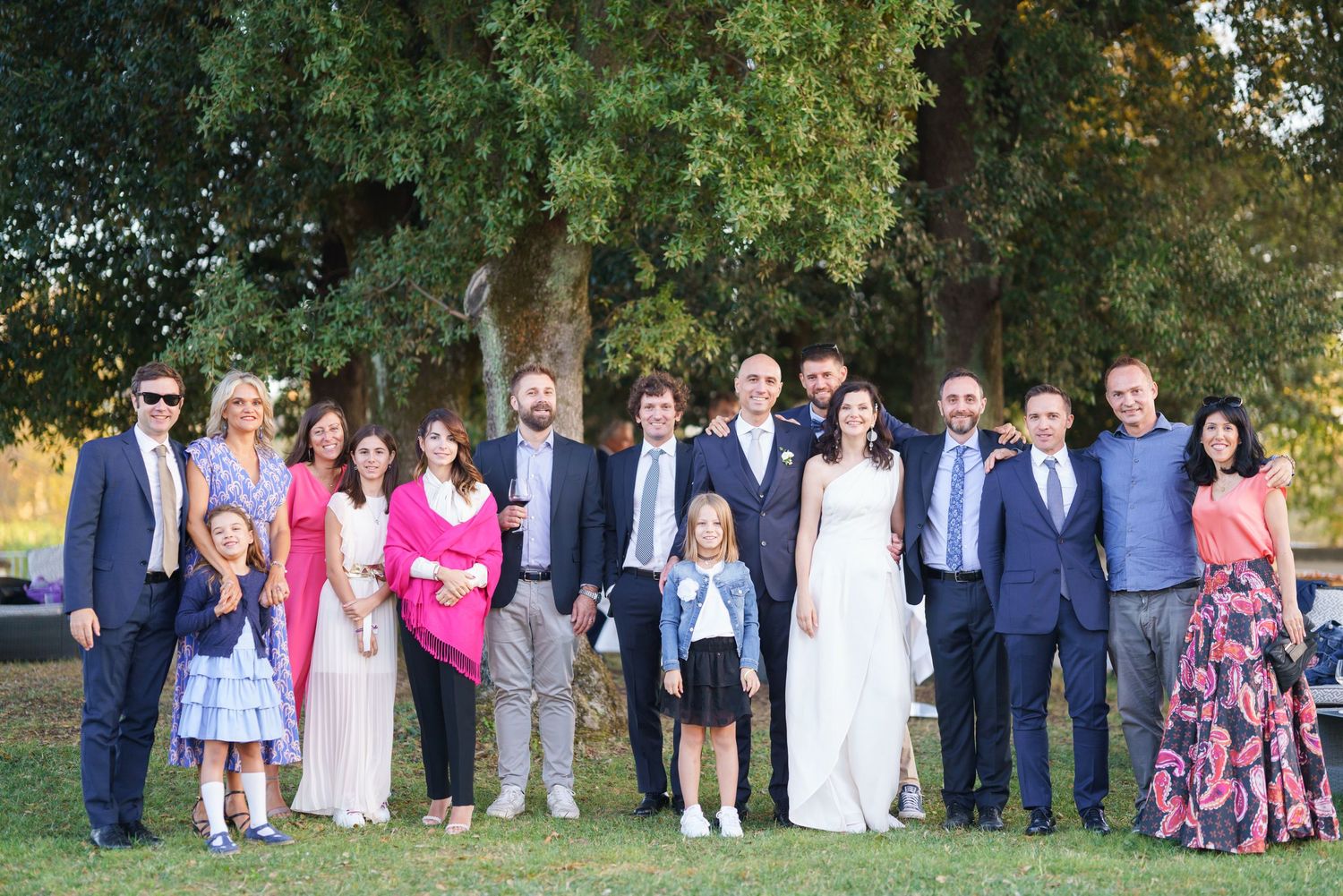 Large wedding party group photo with guests in formal attire standing together outside.