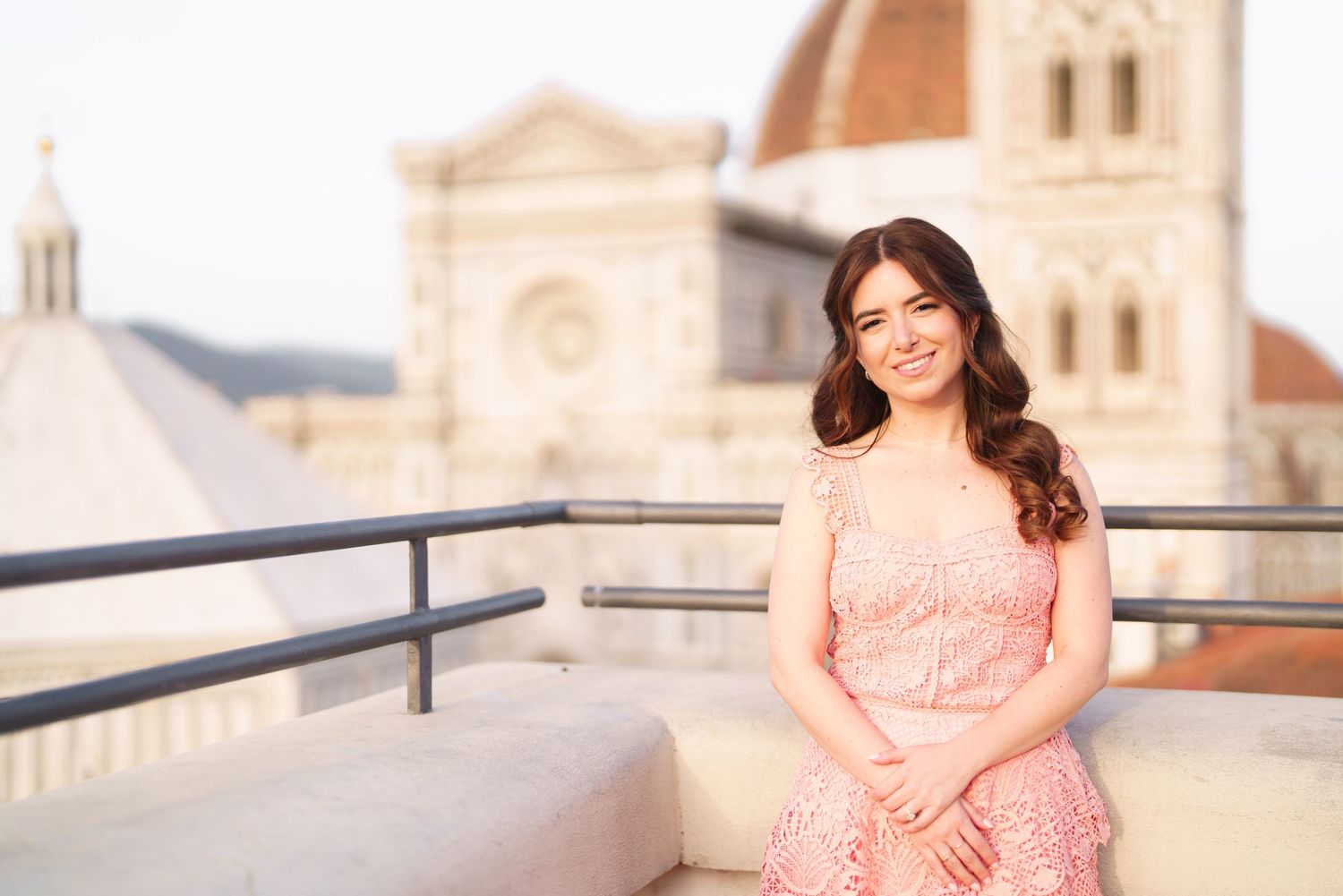 Woman in a peach colored dress poses on a rooftop terrace with European architecture in the background.