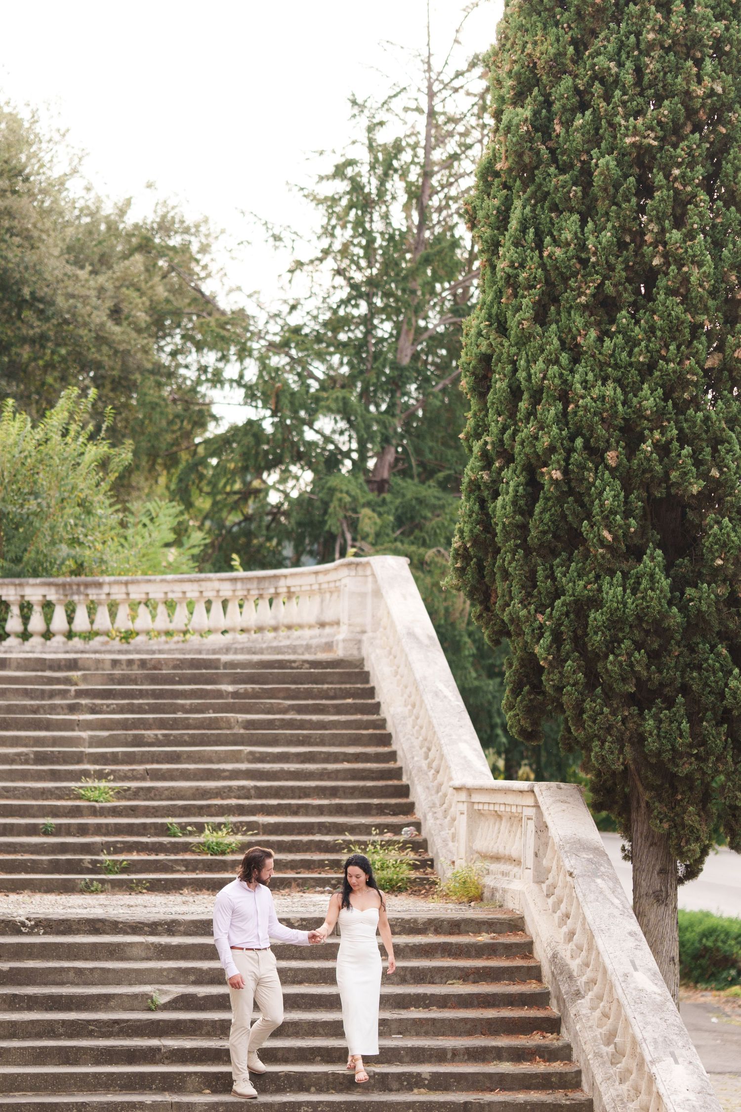 A couple shares a romantic moment on elegant stone garden steps surrounded by lush greenery.