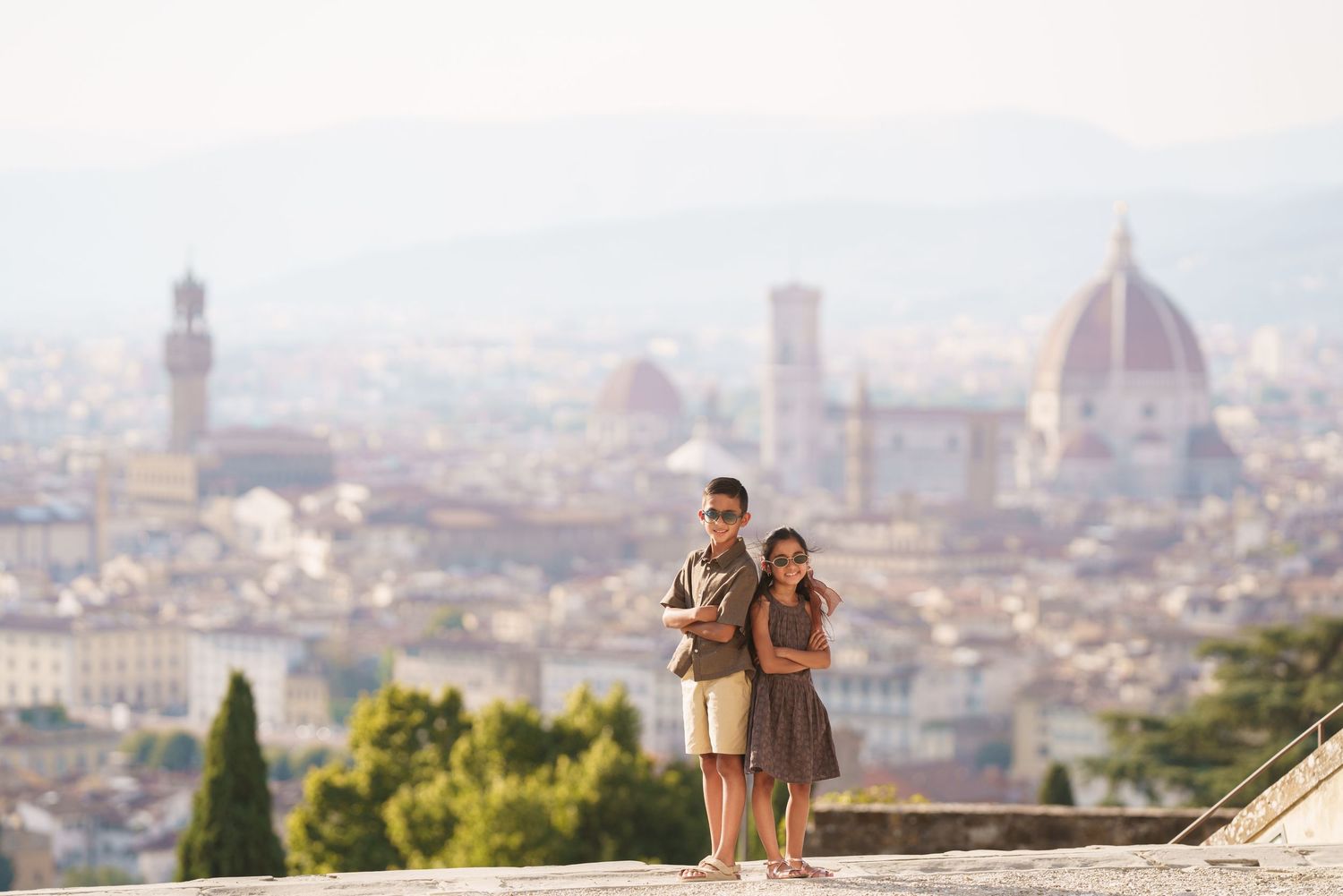 Two children stand on a terrace overlooking the iconic Florence skyline with the Duomo cathedral dome visible behind them.