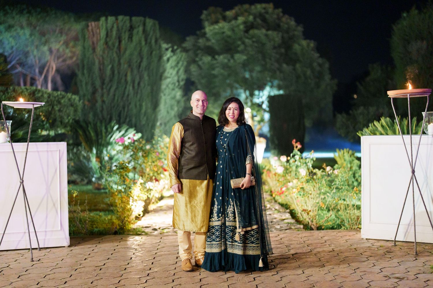 Outdoor evening celebration with guests walking along lit garden paths.