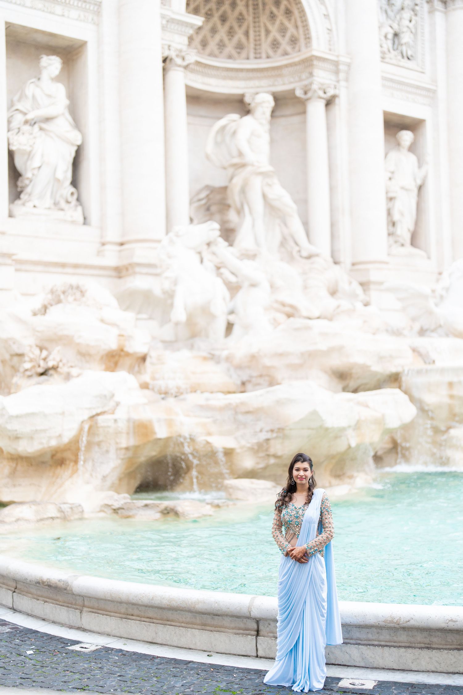 Woman in light blue saree poses in front of the majestic Trevi Fountain in Rome.