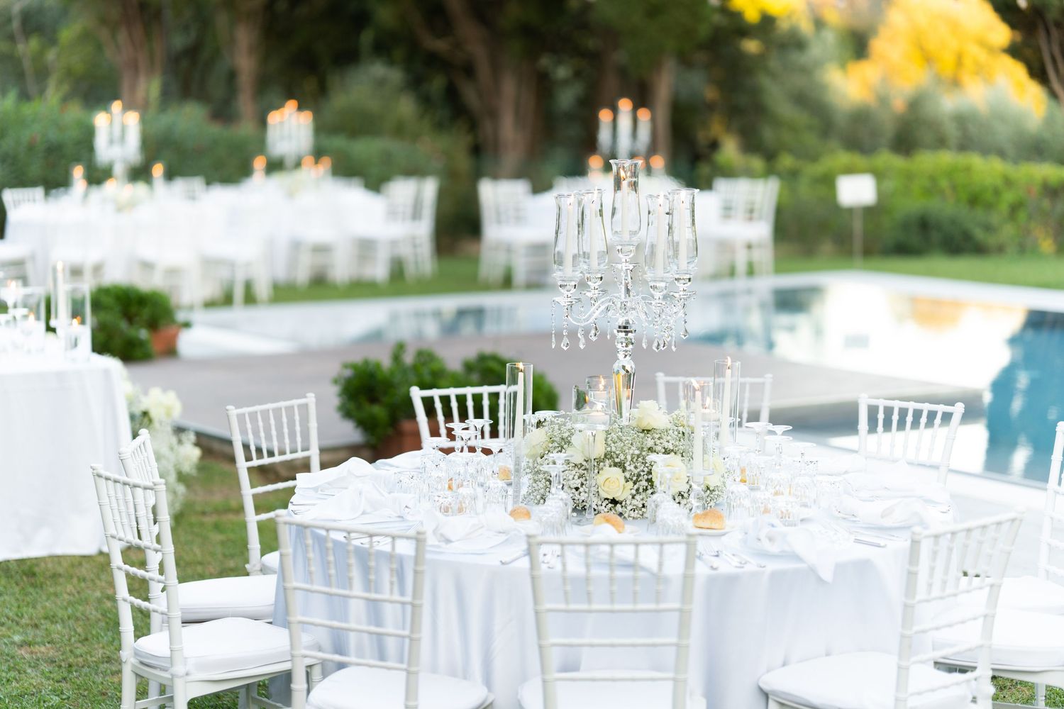 Elegant white wedding reception tables with crystal candelabras beside pool.