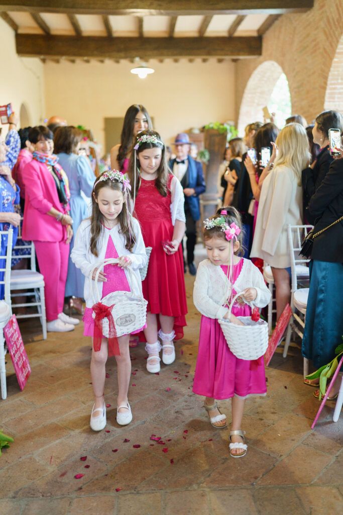 Young attendants in matching pink dresses line up for a wedding ceremony procession.