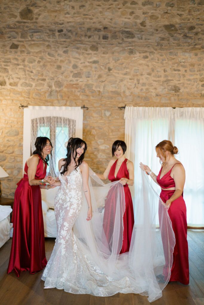 Bridesmaids in red dresses helping adjust the bride's wedding gown and veil.