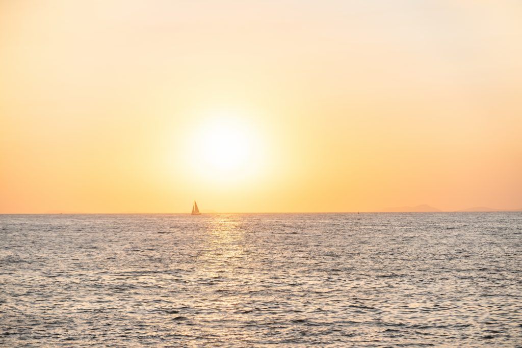 Golden sunset over calm ocean waters with sailing boat silhouette.