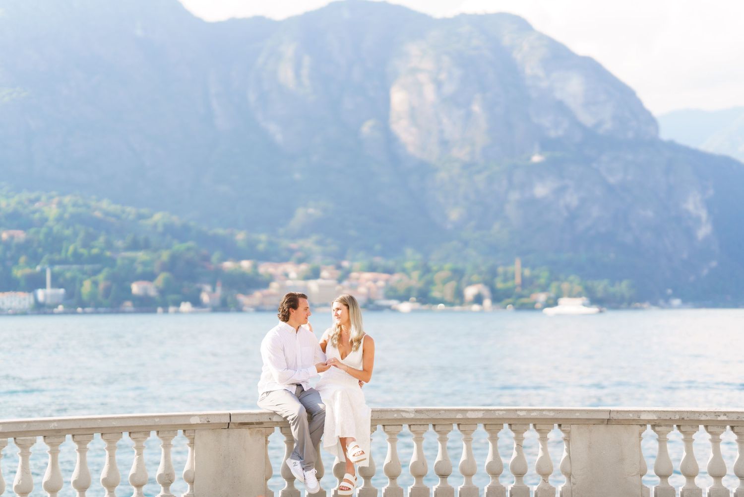 Scenic lakeside wedding ceremony with mountain backdrop and ornate stone balustrade overlooking Lake Como, Italy.
