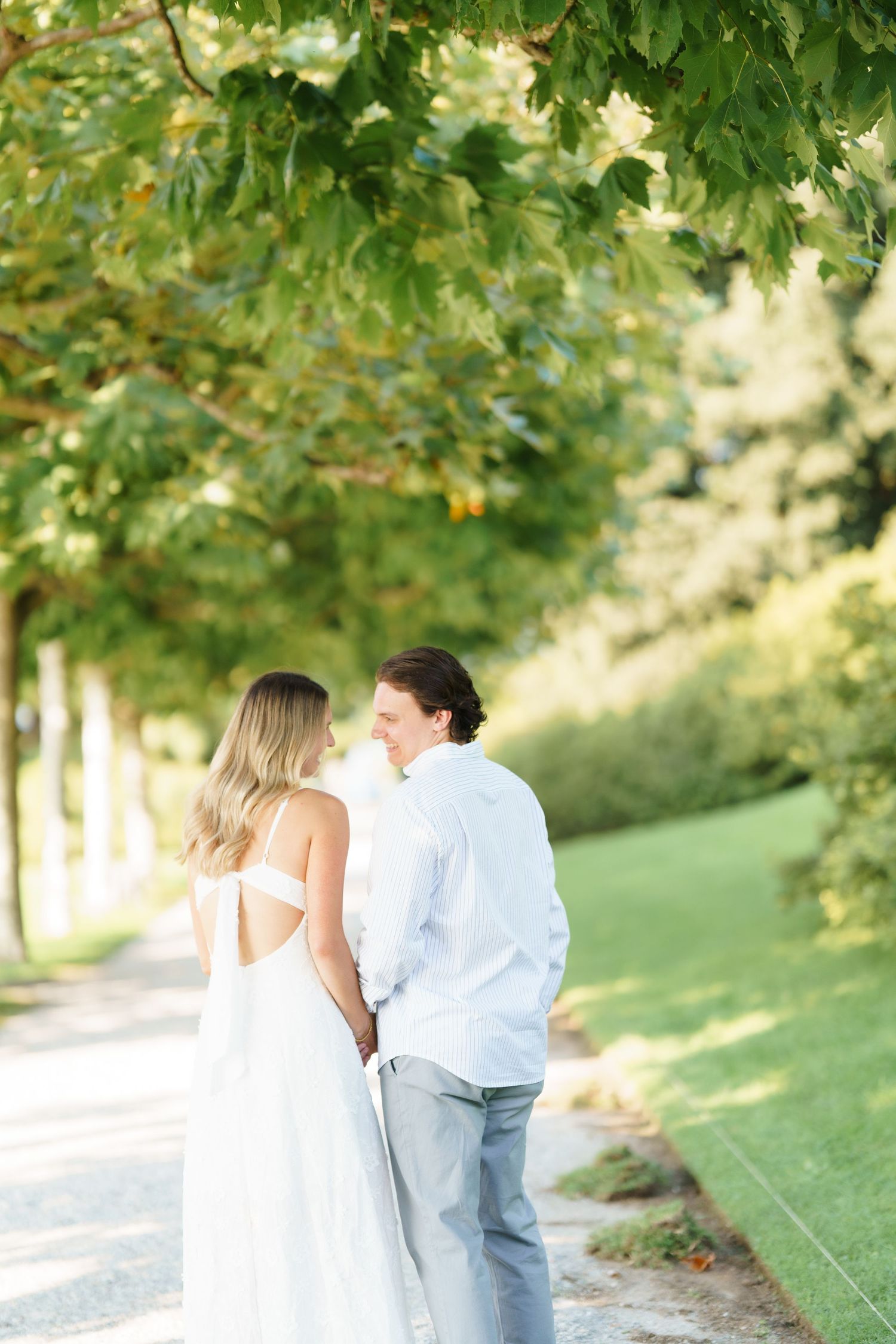 Couple embracing on a path surrounded by lush green trees on a sunny summer day.
