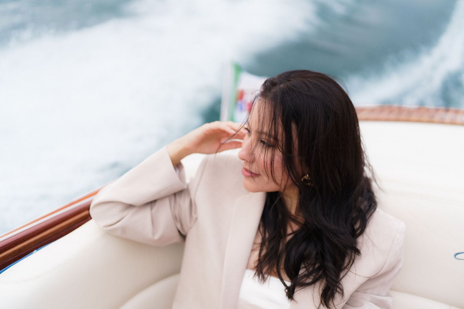 Woman with dark hair in white sweater relaxing on boat with turquoise water in background.