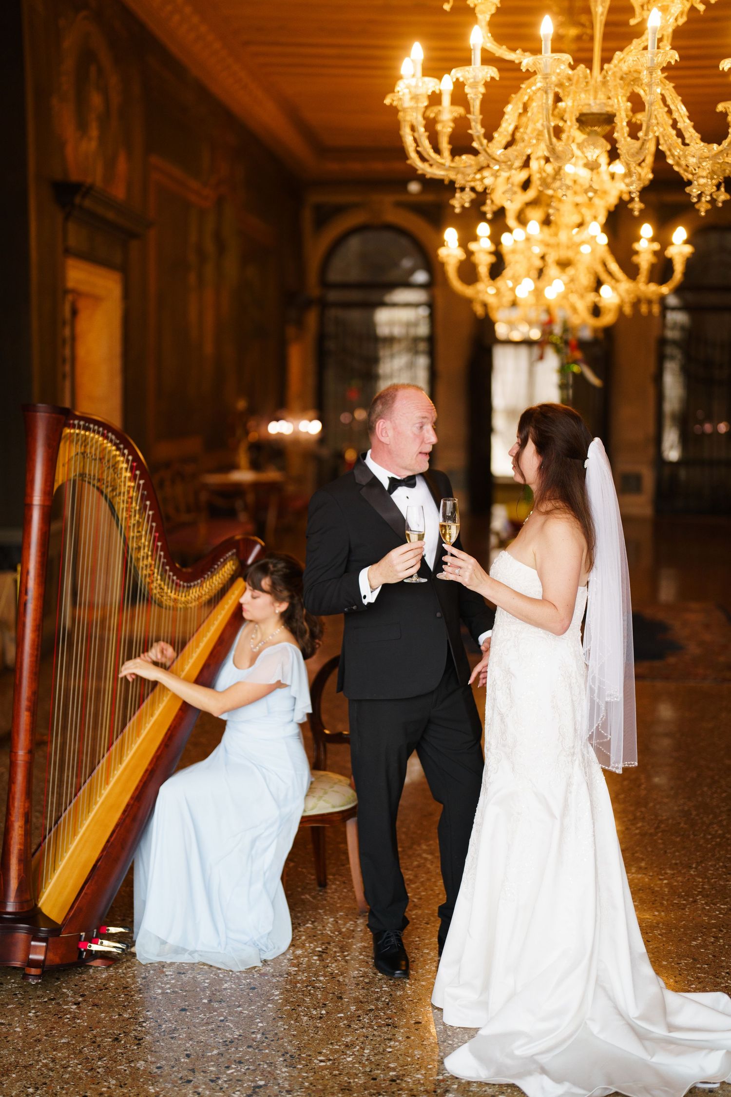 A couple dances elegantly in a grand ballroom with ornate chandeliers and a harpist providing romantic ambiance.