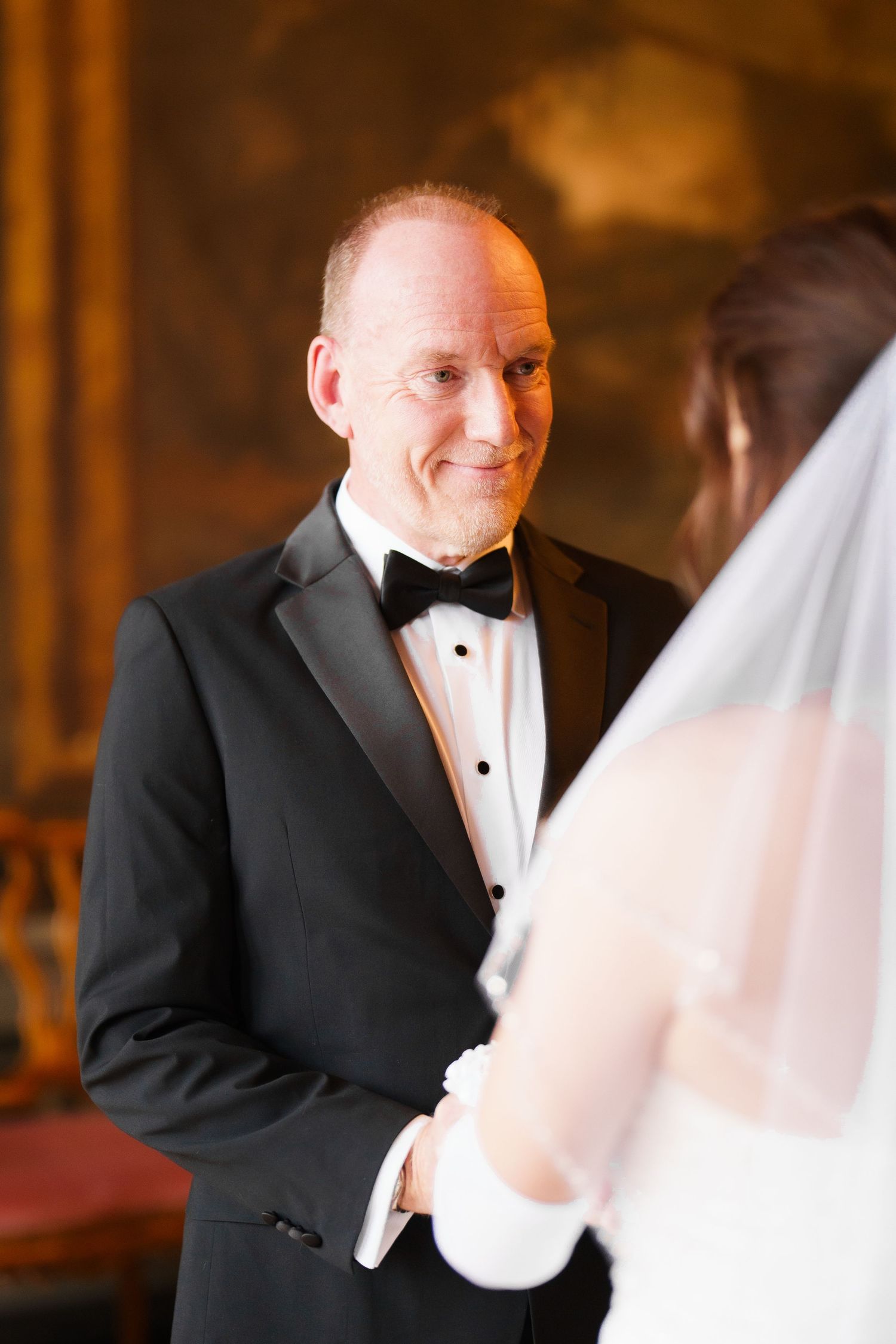 A groom in a black tuxedo and bow tie shares a candid moment with his bride in a white wedding dress.