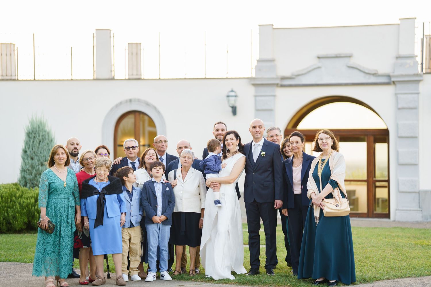 Group of wedding guests lined up for photos outside a white church with arched doorway.