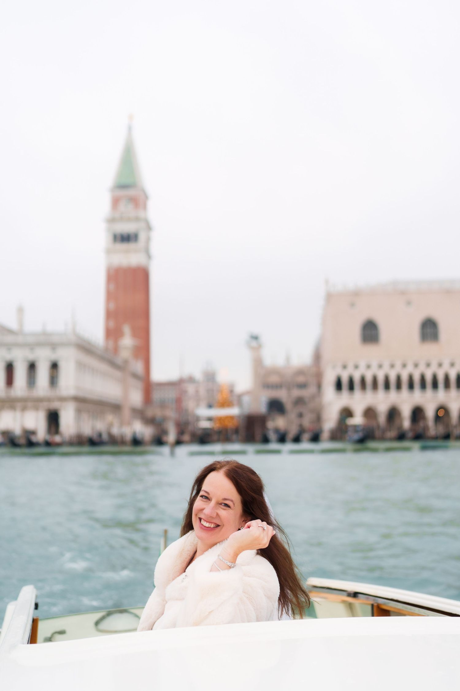 View of Venice's iconic St Mark's Square and campanile tower from a boat on the turquoise waters of the lagoon.