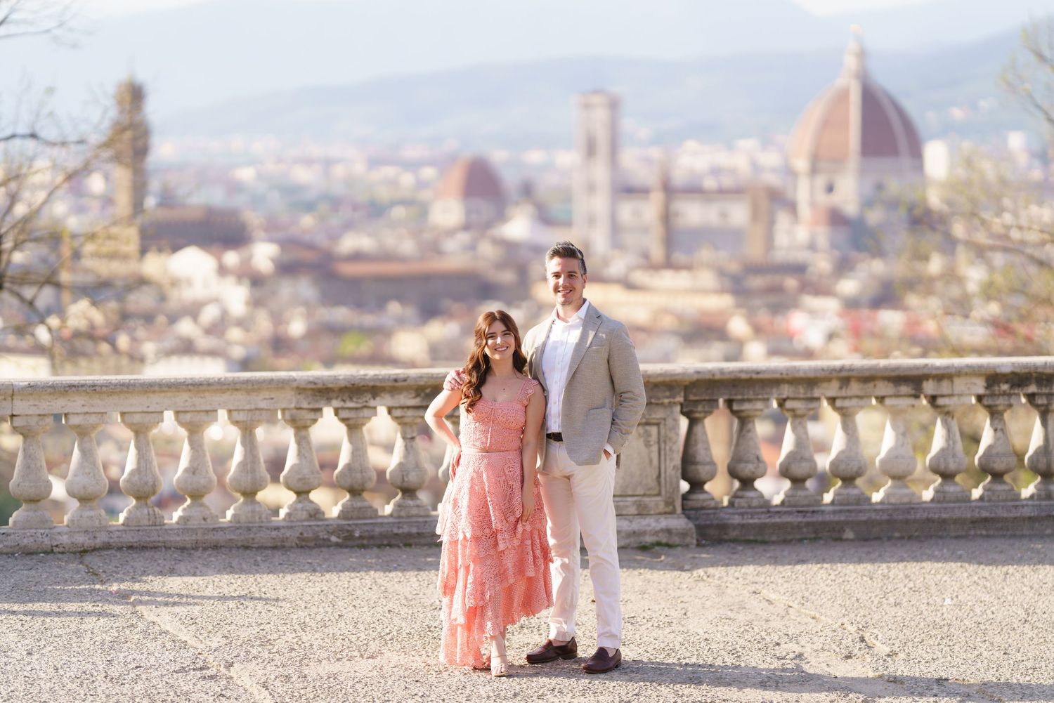 A couple poses at a scenic overlook in Florence, Italy with the iconic Duomo cathedral visible in the background.