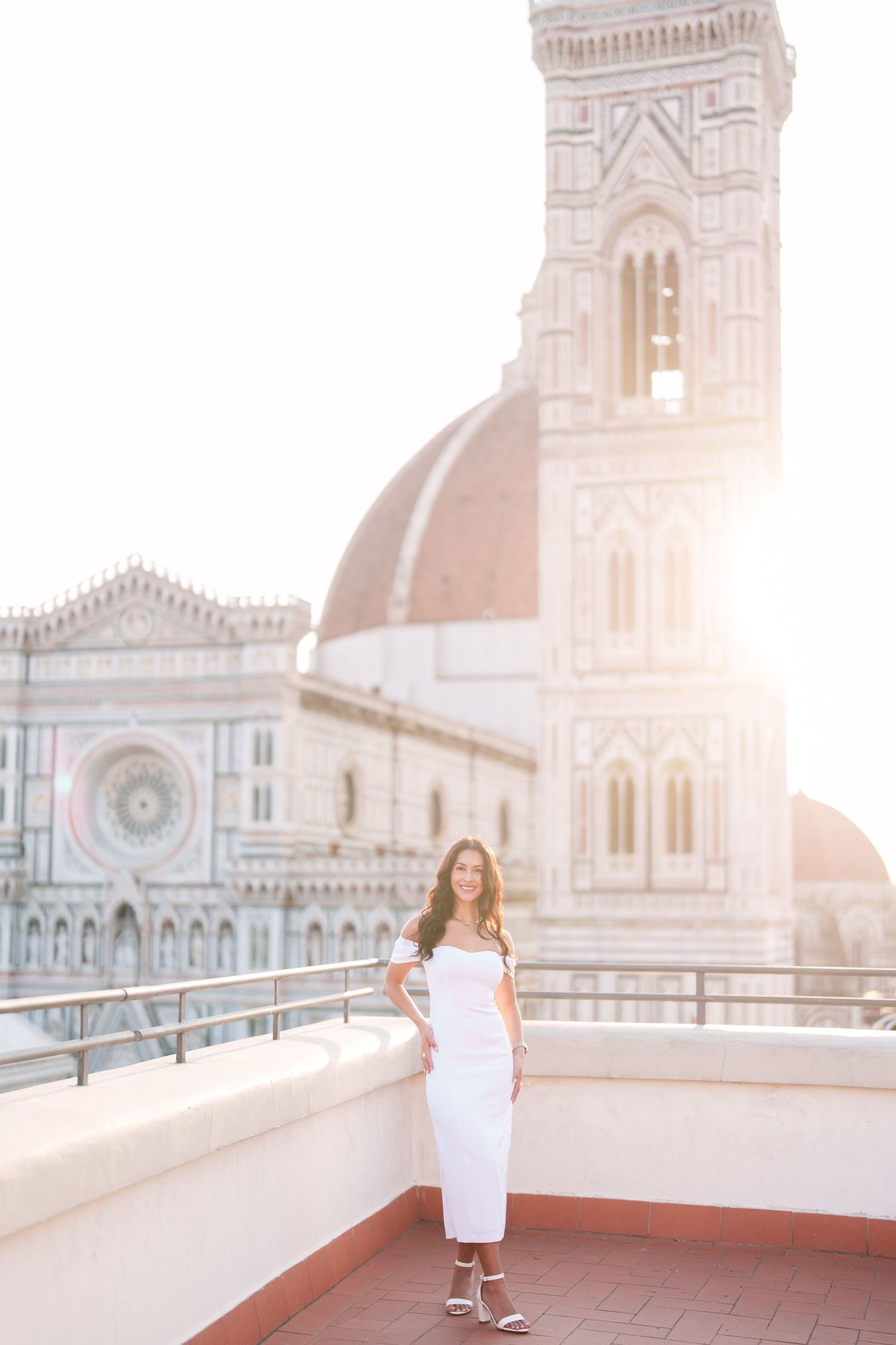 A scenic rooftop view of Florence Cathedral's iconic dome and tower at sunset with a woman in a white dress.