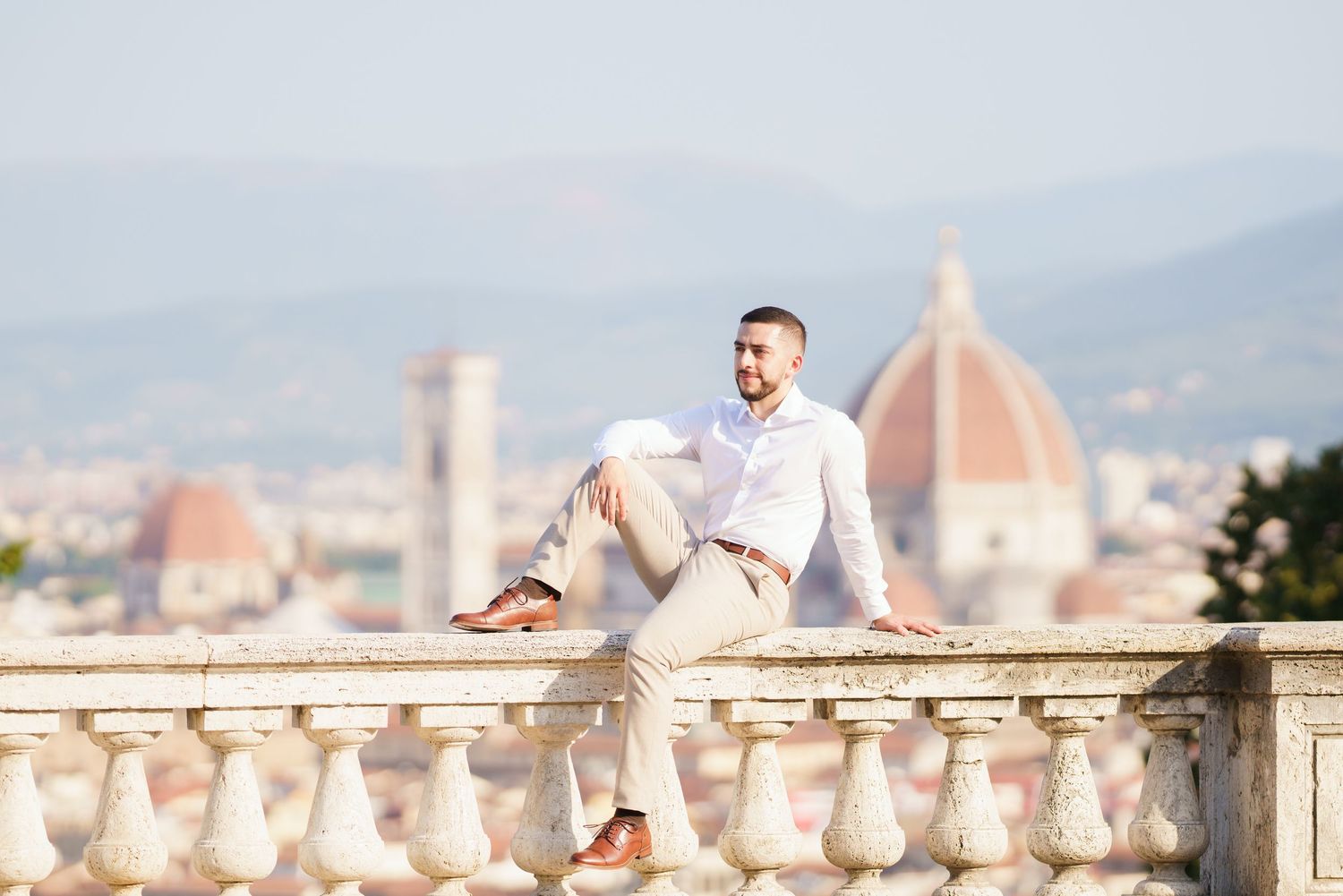 Person in white outfit sits on stone balustrade overlooking Florence with Duomo cathedral visible in background.