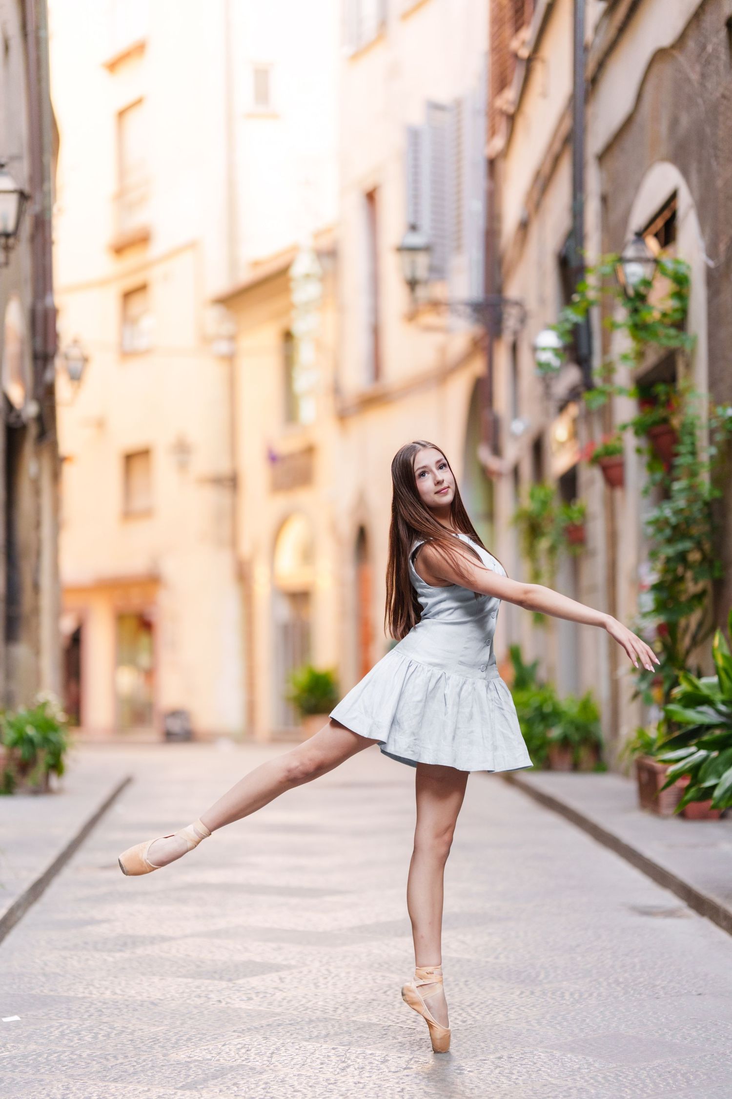 Ballet dancer in white dress performs graceful poses on a charming European cobblestone street.