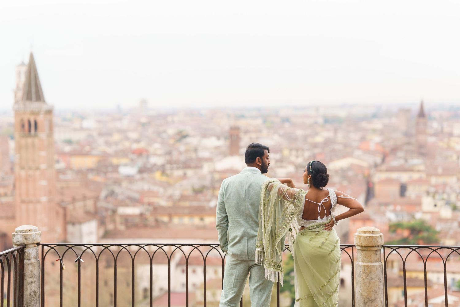 Two people in matching outfits enjoy a scenic view of a European cityscape from a hilltop viewpoint.