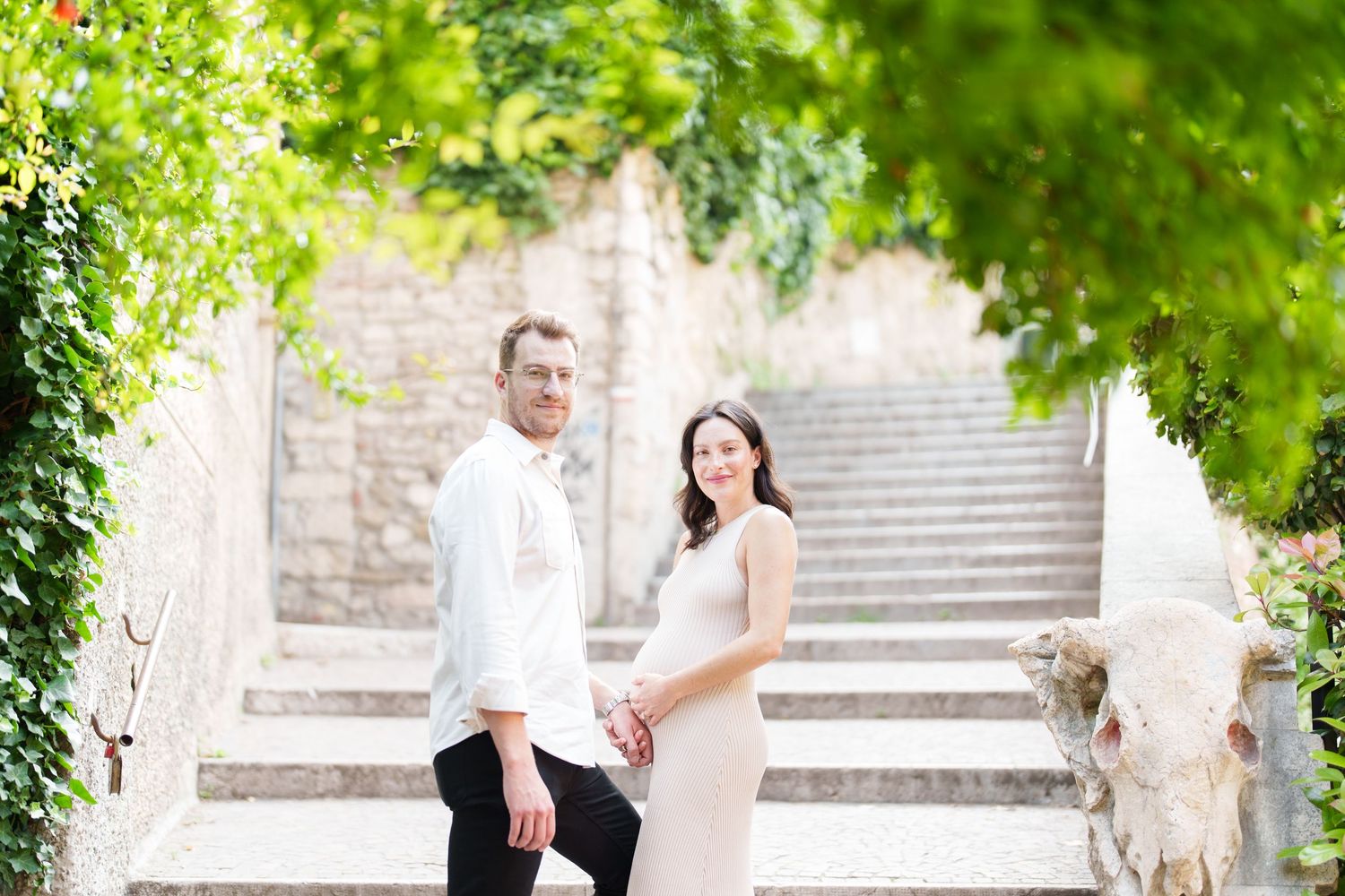 Couple shares romantic moment on stone steps surrounded by lush green foliage in outdoor garden setting.