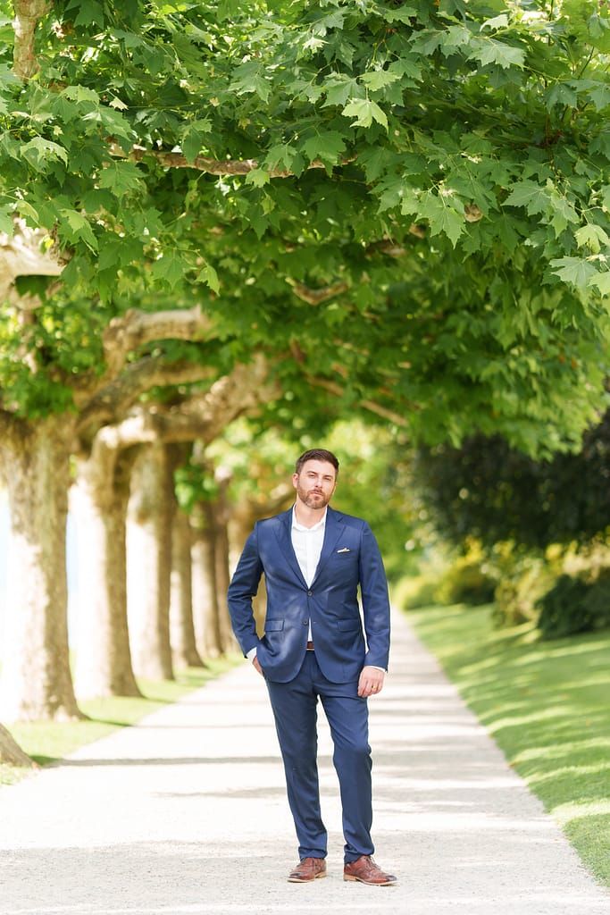 A person in a navy blue suit poses on a tree-lined path in a series of progressive walking shots.