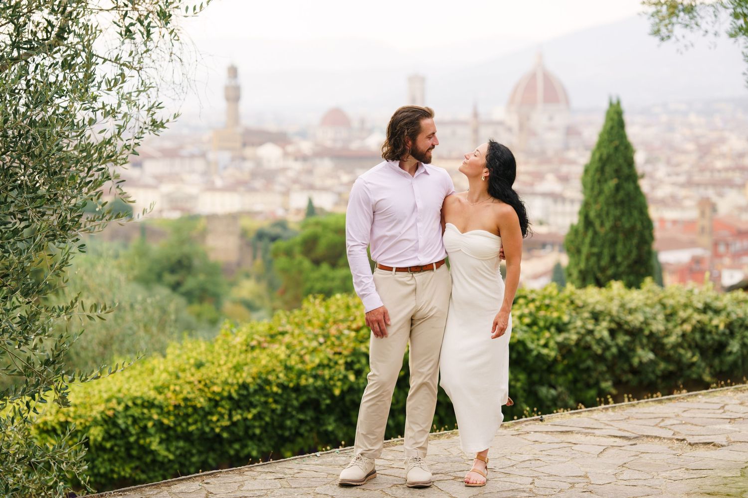 A couple in white clothing admires the scenic view of Florence, Italy with the Duomo cathedral visible in the distance.