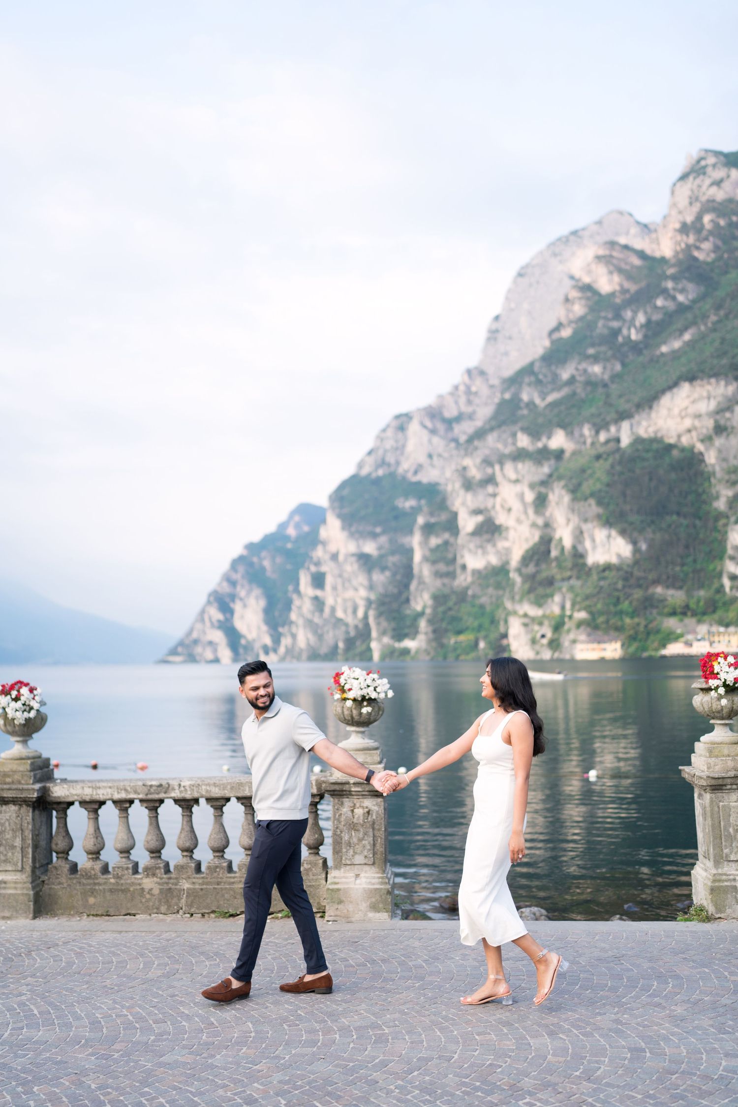 Couple dancing on a stone terrace overlooking Lake Garda in Italy with dramatic mountain cliffs in the background.