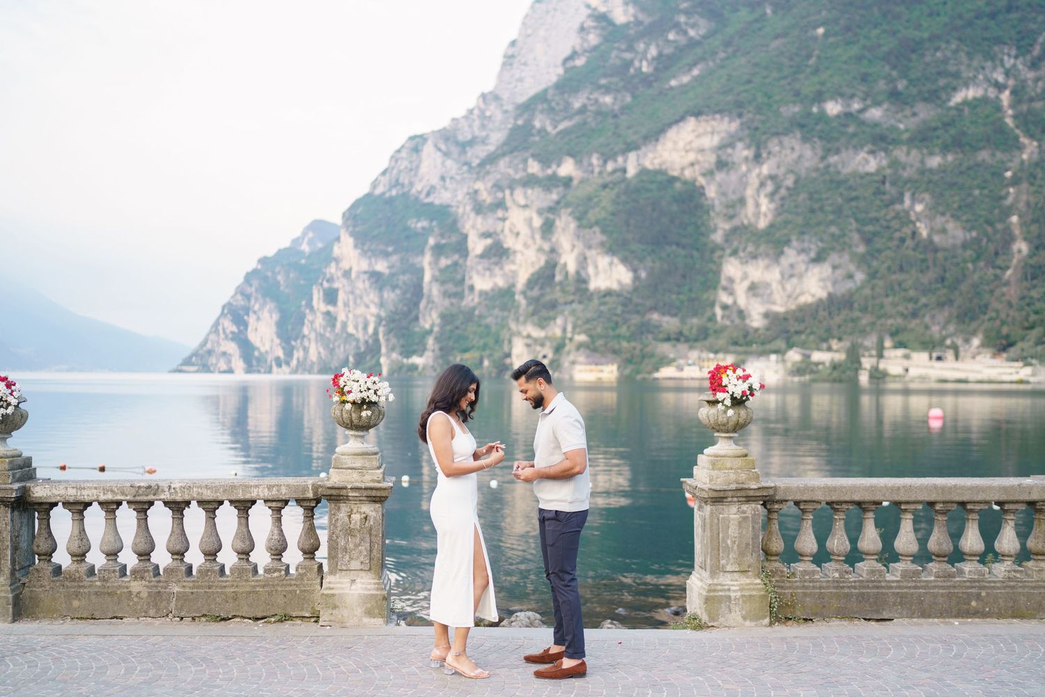 A scenic mountain lake view with cliffs and people standing on a stone balcony overlooking the water.