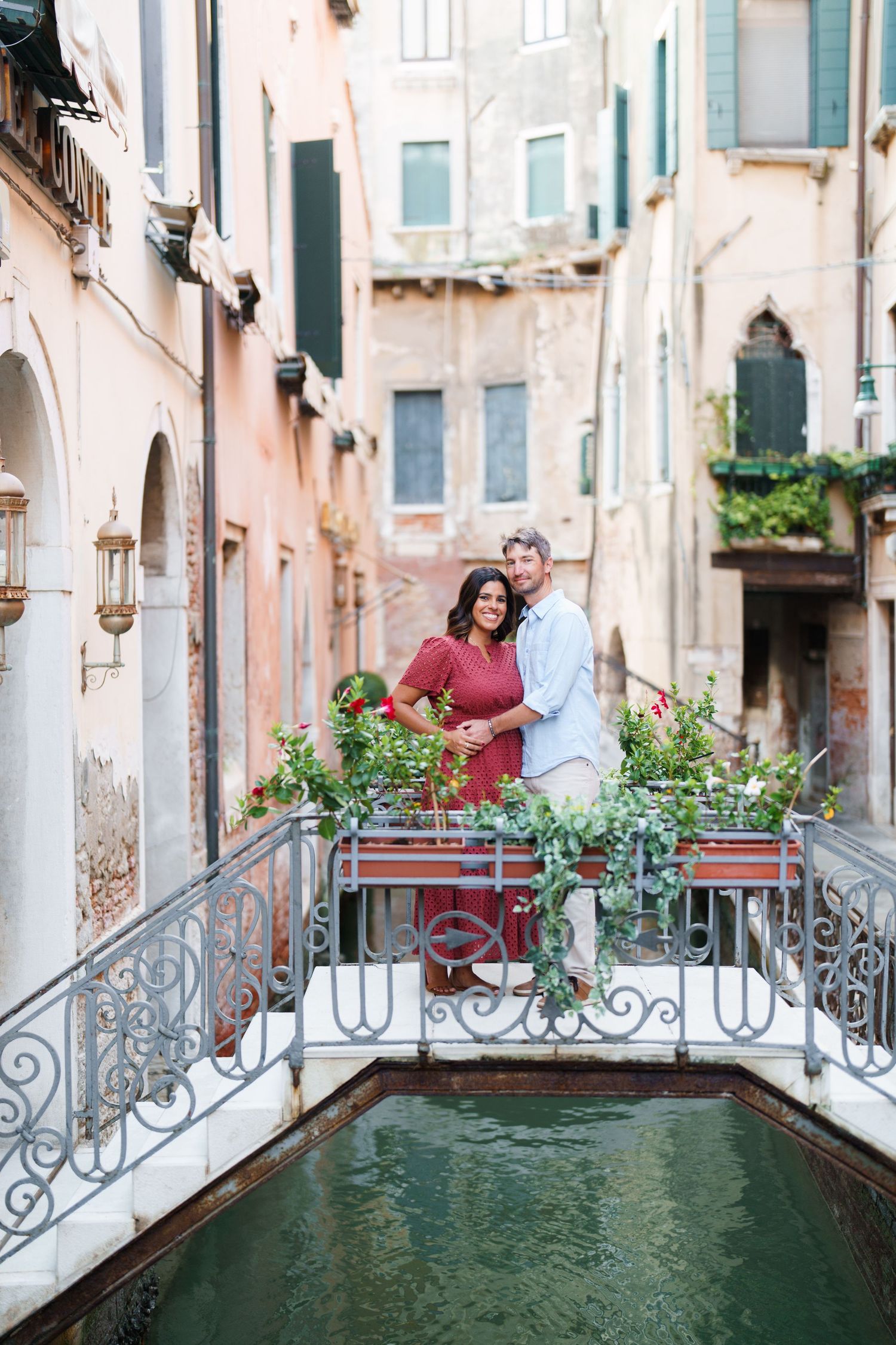 Romantic couple embracing on a Venetian bridge over a canal, surrounded by colorful flowers and historic buildings in Venice, Italy.