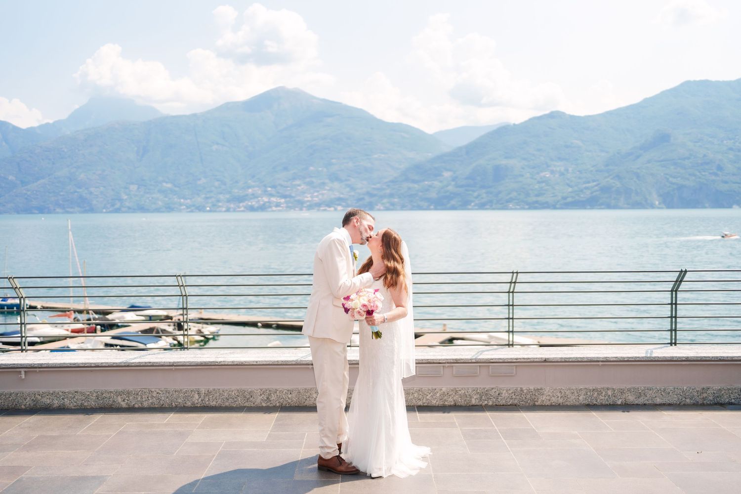 Bride and groom share a kiss on a lakeside terrace with stunning mountain views at Lake Como wedding.