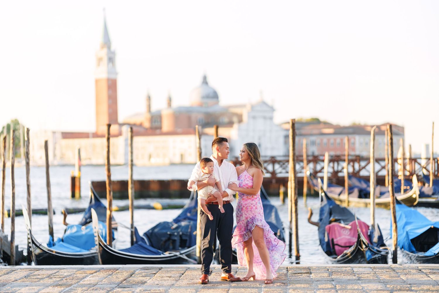 Family posing with gondolas and San Giorgio Maggiore church in background at Venice waterfront.