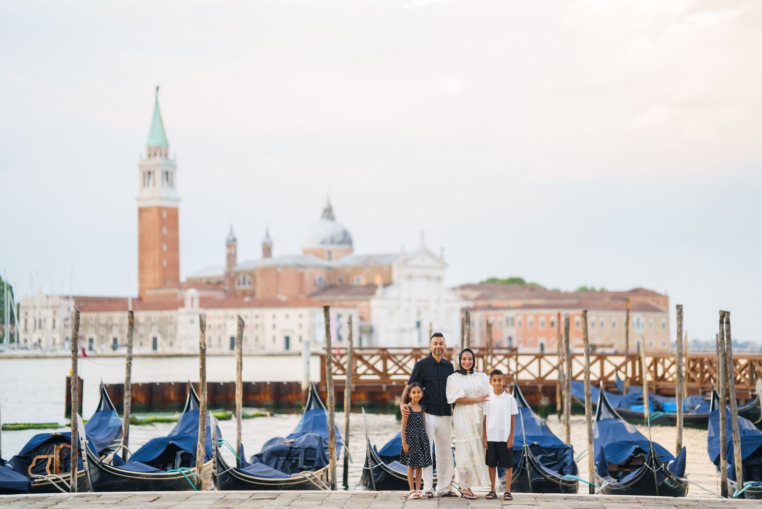 Family posing by gondolas in Venice with San Giorgio Maggiore church in the background.