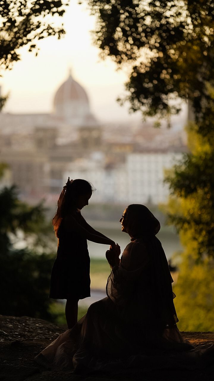 Silhouette of mother and daughter holding hands with Florence cathedral dome in soft bokeh background.