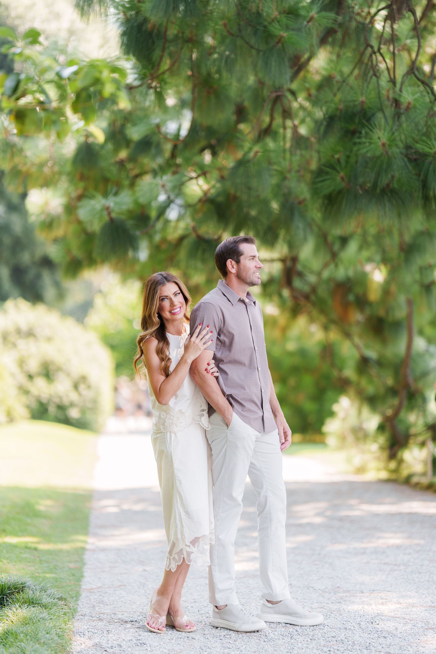 A couple poses together on a garden path, woman in white dress Family photographer in Bellagio, Varenna and Lake Como