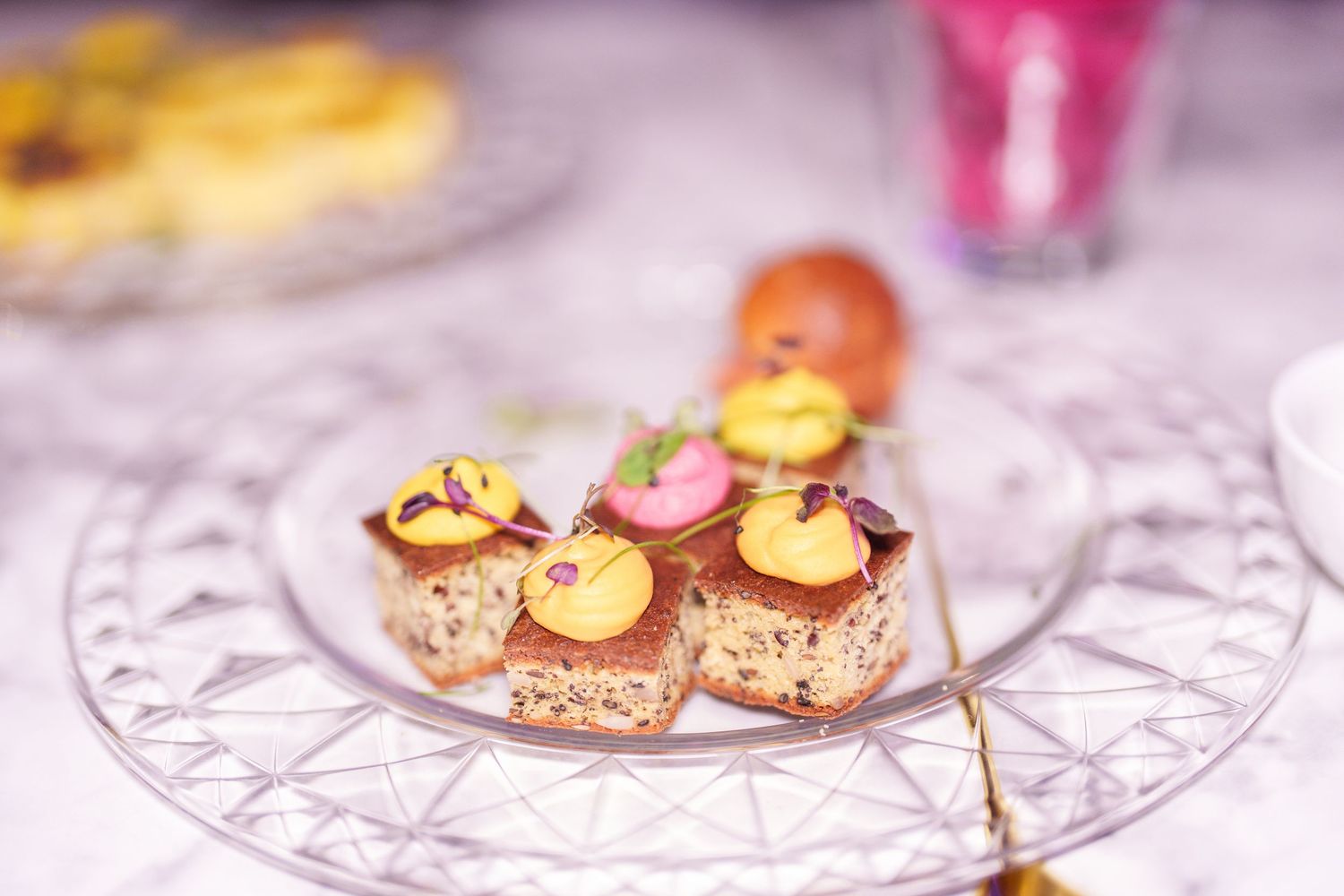 Elegant petit fours with yellow and pink decorations on a crystal glass plate at a formal event.