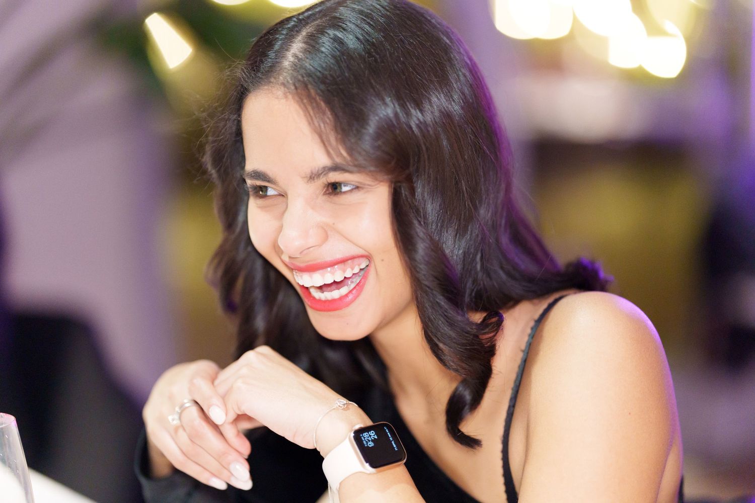 Smiling woman wearing a black dress and smartwatch, laughing joyfully at an elegant event.