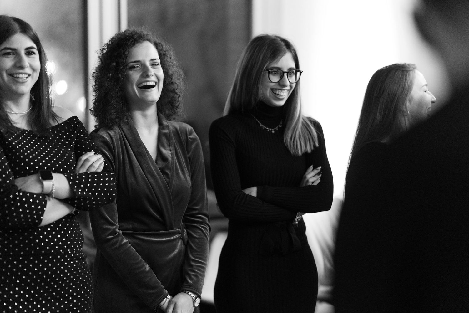Black and white photo of three smiling women standing with arms crossed at a professional networking event.