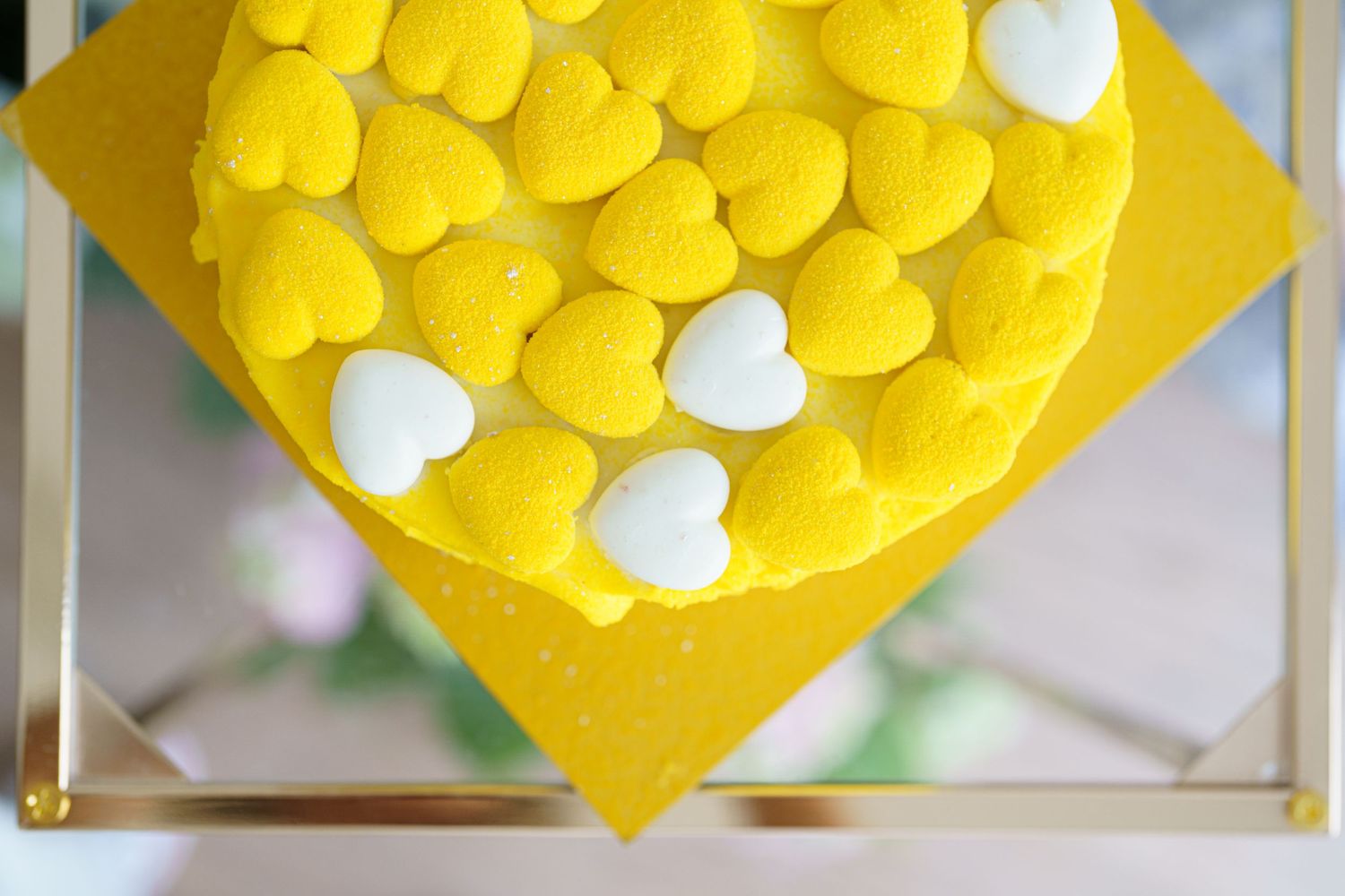 Yellow heart-shaped macarons arranged on a yellow polka dot surface with a few white heart macarons as accents.