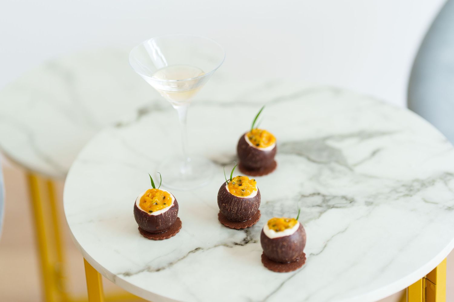 Elegant chocolate dessert bites topped with passion fruit on a marble table beside a martini glass.