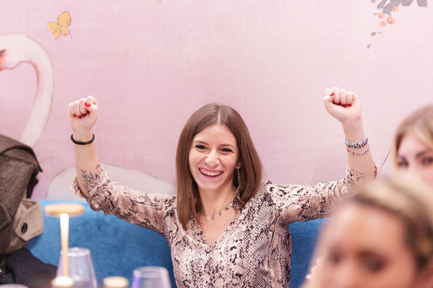 Excited young woman celebrating with arms raised in a pink decorated restaurant setting.